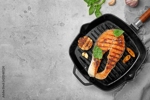 Frying pan with tasty salmon steak on grey background