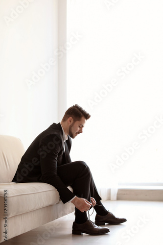 Young man putting on elegant leather shoes indoors