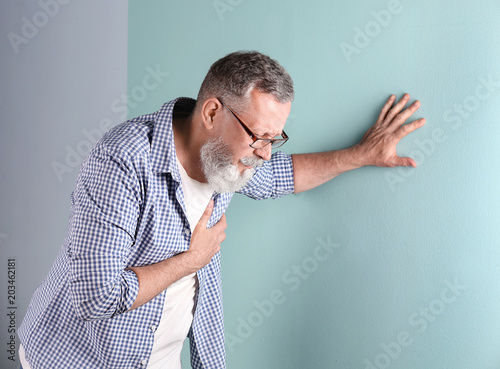 Canvas Print Mature man having heart attack on color background
