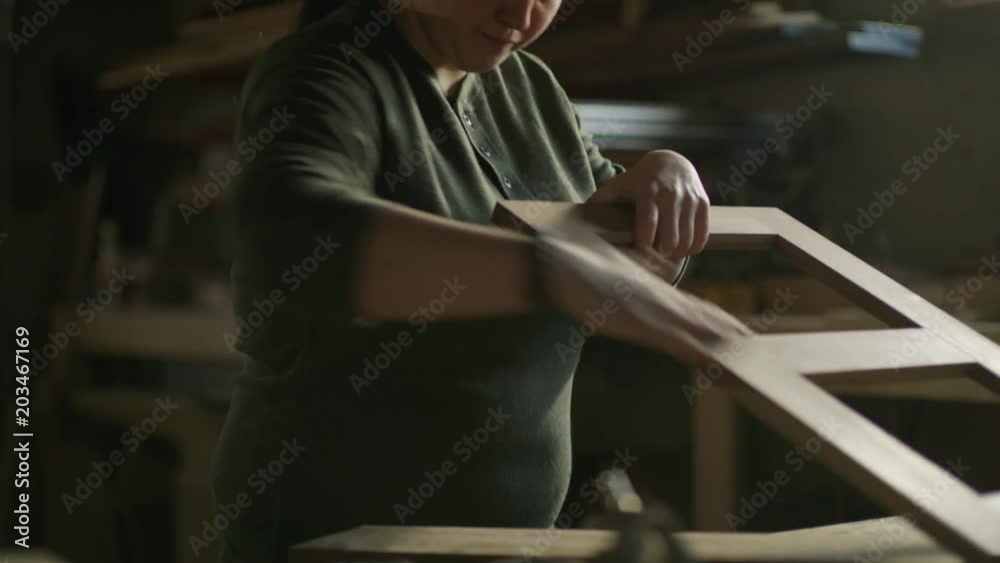 Slow motion tilt up on woman sanding wood frame in workshop / Provo, Utah, United States Slow motion tilt up on woman sanding wood frame in workshop / Provo, Utah, United States