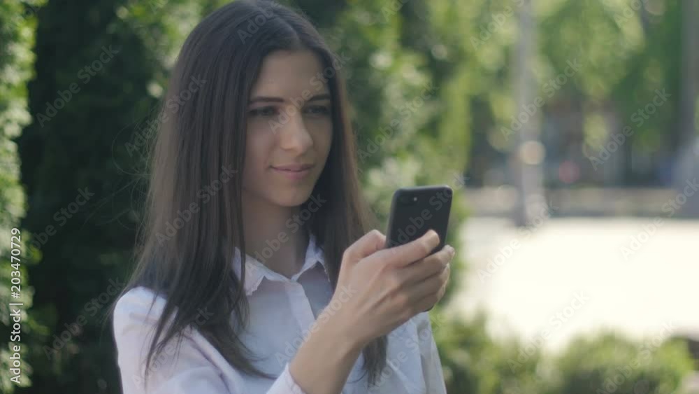 portrait of a young woman in a white shirt uses a smartphone in the afternoon on a street in the city. portrait of a young woman in a white shirt uses a smartphone in the afternoon on a street in the city.