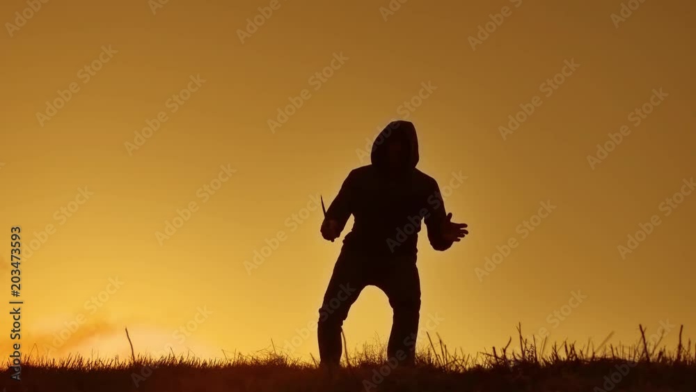 silhouette of a man in a hood with a knife. Shadow blur of horror man in jacket with hood facing side lifestyle body and show the knife in his hand. A dangerous thug with a knife killer bandit silhouette of a man in a hood with a knife. Shadow blur of horror man in jacket with hood facing side lifestyle body and show the knife in his hand. A dangerous thug with a knife killer bandit
