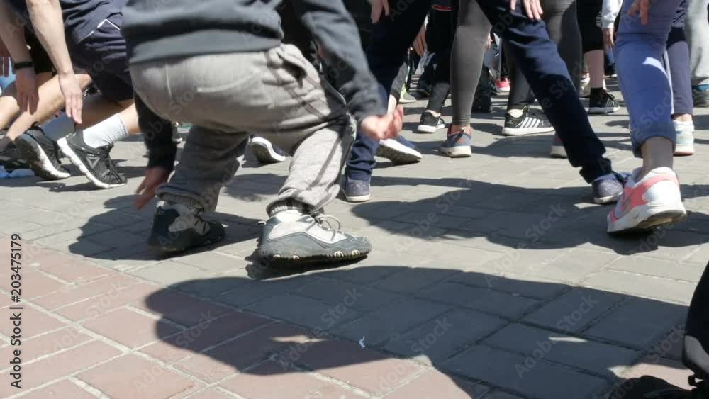 April 21, 2018 - Kamenskoye, Ukraine: large number of people's legs make a warm-up before the marathon race. Jumps and squats of a large number of people in the square April 21, 2018 - Kamenskoye, Ukraine: large number of people's legs make a warm-up before the marathon race. Jumps and squats of a large number of people in the square