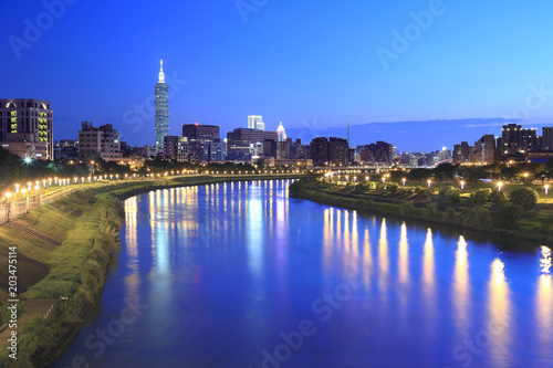 Night view of Taipei City by riverside with skyscrapers and beautiful lights reflecting on smooth water ~ Landmarks of Taipei 101 Tower, Keelung River & Xinyi District in downtown area at dusk