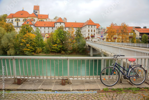 Εκτύπωση καμβά A bicycle parking by Lech River with the majestic Hohes Schloss Castle in the ba