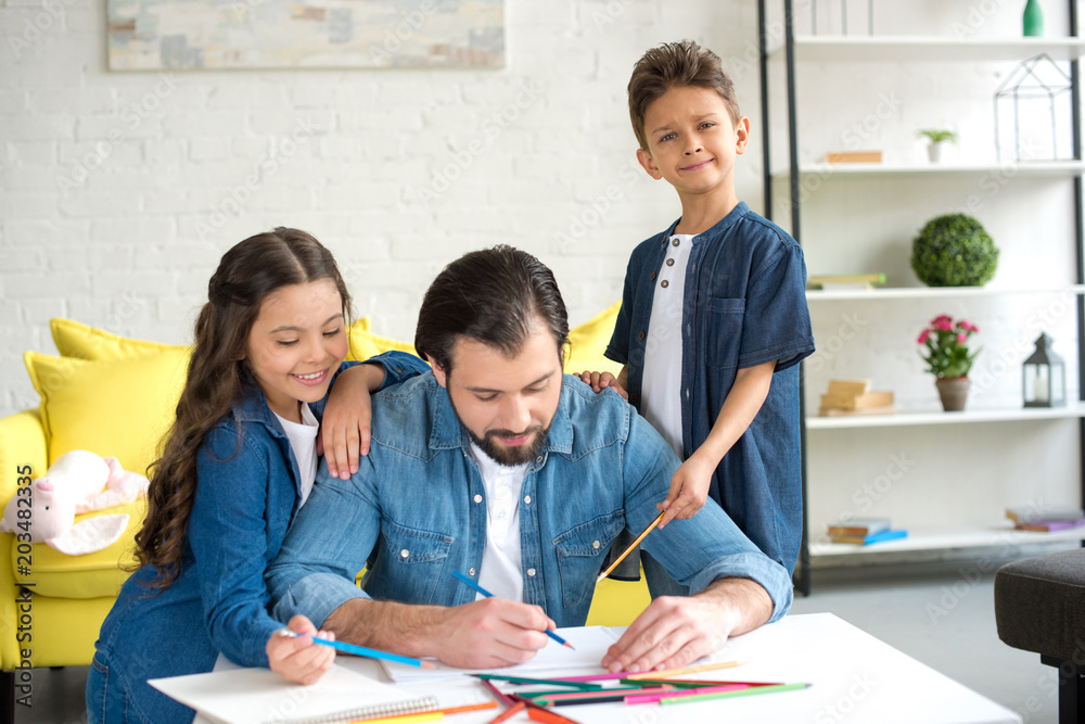 cute happy kids looking at father drawing with colored pencils at home