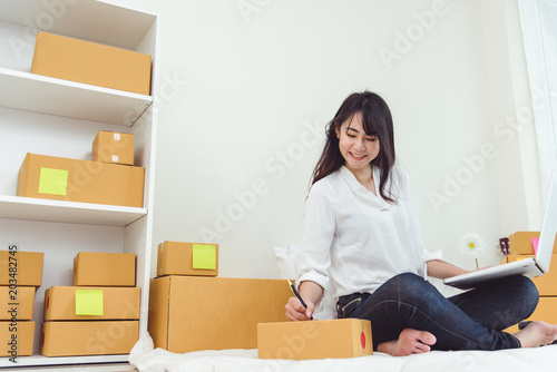 Beauty Asian woman using laptop and start up small business entrepreneur SME and checking order list in bedroom, Young happy freelance woman shopping online marketing or sending parcel to customers © Shutter2U