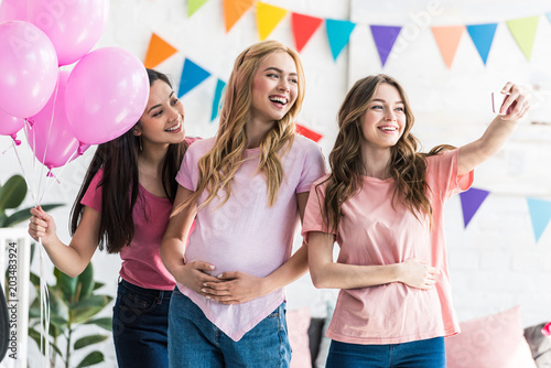 multicultural friends and pregnant woman taking selfie with smartphone at baby-party