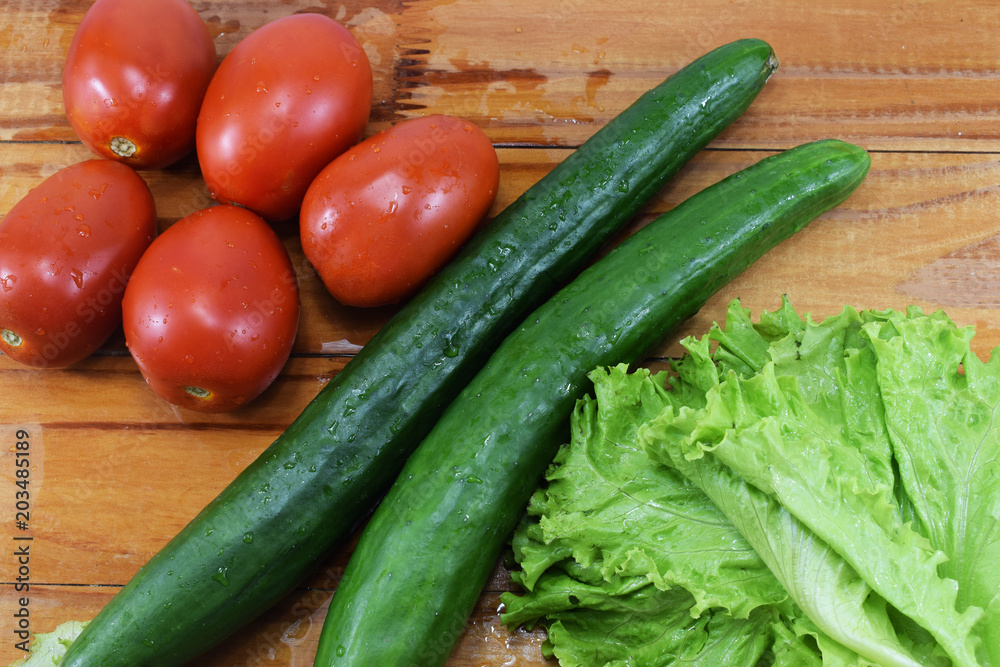 fresh juicy red tomatoes, cucumbers and lettuce on a wooden table fresh juicy red tomatoes, cucumbers and lettuce on a wooden table