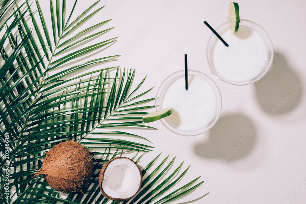 top view of organic coconuts, green palm leaves and coconut cocktails in glasses with drinking straws on white top view of organic coconuts, green palm leaves and coconut cocktails in glasses with drinking straws on white