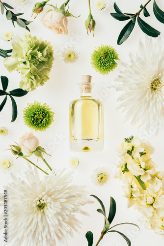 top view of bottle of aromatic perfume surrounded with flowers and green branches on white photo