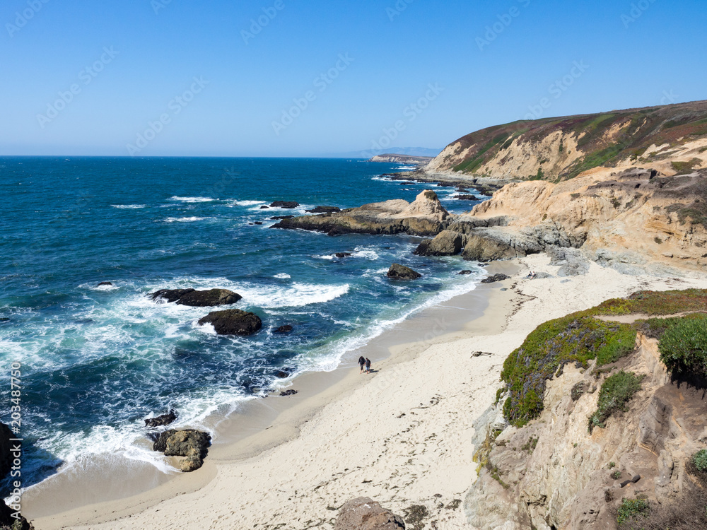 Barefoot hikers on beach below rocky cliffs and waves along shore in Bodea Head, Marin County, California, United States
