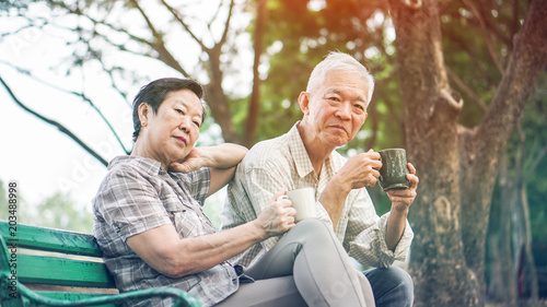 Asian senior couple relax drinking coffee in summer park, green nature © glowonconcept