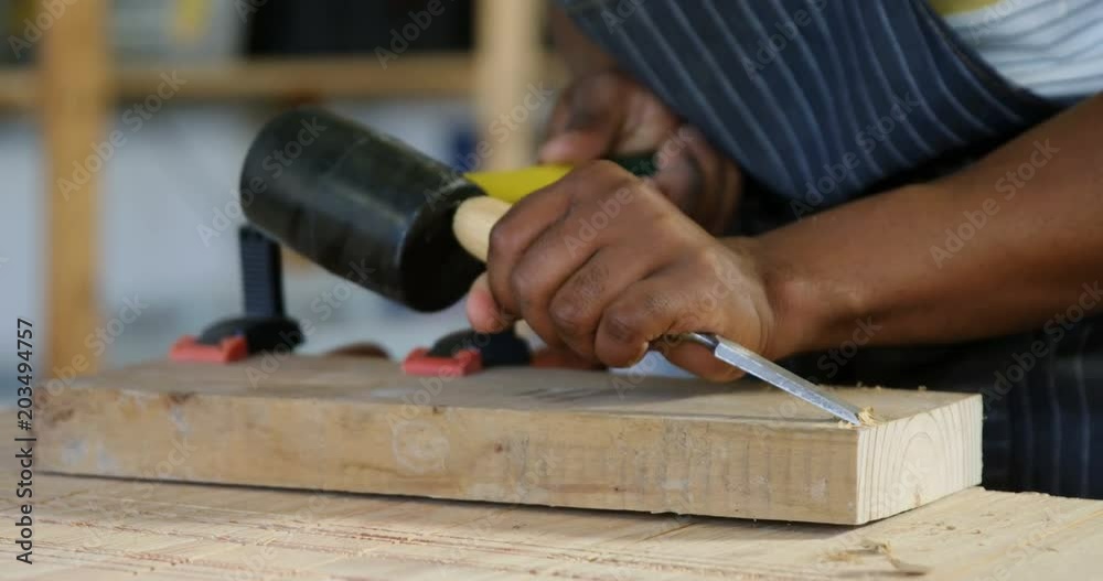 Mid section of carpenter carving wood with hammer at table Mid section of carpenter carving wood with hammer at table