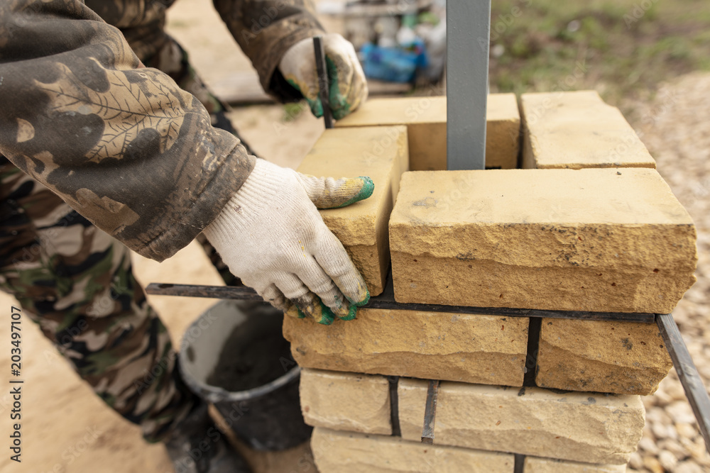 Fototapeta man builds a brick wall at a construction site