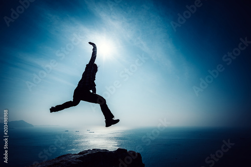 hiker jumping on sunrise seaside cliff edge
