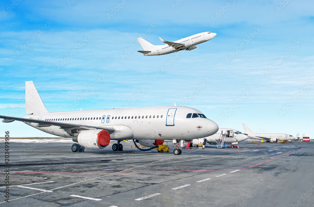 Passenger aircraft row, airplane parked on service before departure at the airport. One aircraft take off to runway in the cloudy sky. Passenger aircraft row, airplane parked on service before departure at the airport. One aircraft take off to runway in the cloudy sky.