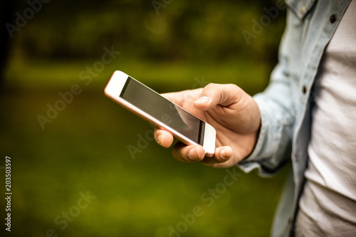 Young man in park using mobile phone. Focus is on hand. Close up.