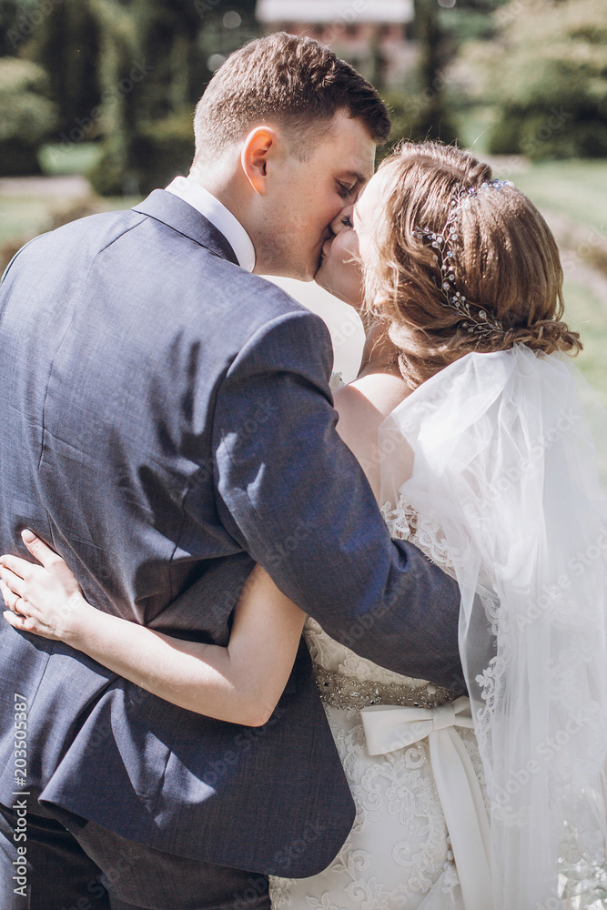 Fototapeta premium beautiful gorgeous bride and groom kissing in sunny spring park and enjoying day. happy wedding couple relaxing in green garden. happy marriage moments. elopement concept