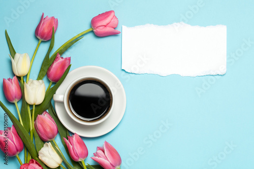 Cup of coffe and pink tulips on blue background.