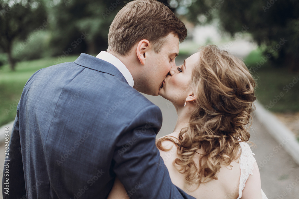 beautiful gorgeous bride and groom walking in sunny park and kissing. happy wedding couple hugging in green garden at old castle. happy romantic moments. elopement concept beautiful gorgeous bride and groom walking in sunny park and kissing. happy wedding couple hugging in green garden at old castle. happy romantic moments. elopement concept