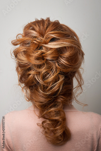 Hairstyle Greek braid on the head of a red hair woman back view close-up on a gray background.
