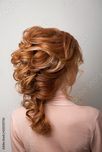 Hairstyle Greek braid on the head of a red hair woman back view close-up on a gray background.
