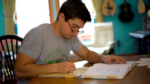 Low angle side shot of teenage boy doing math homework at dining room table. photo