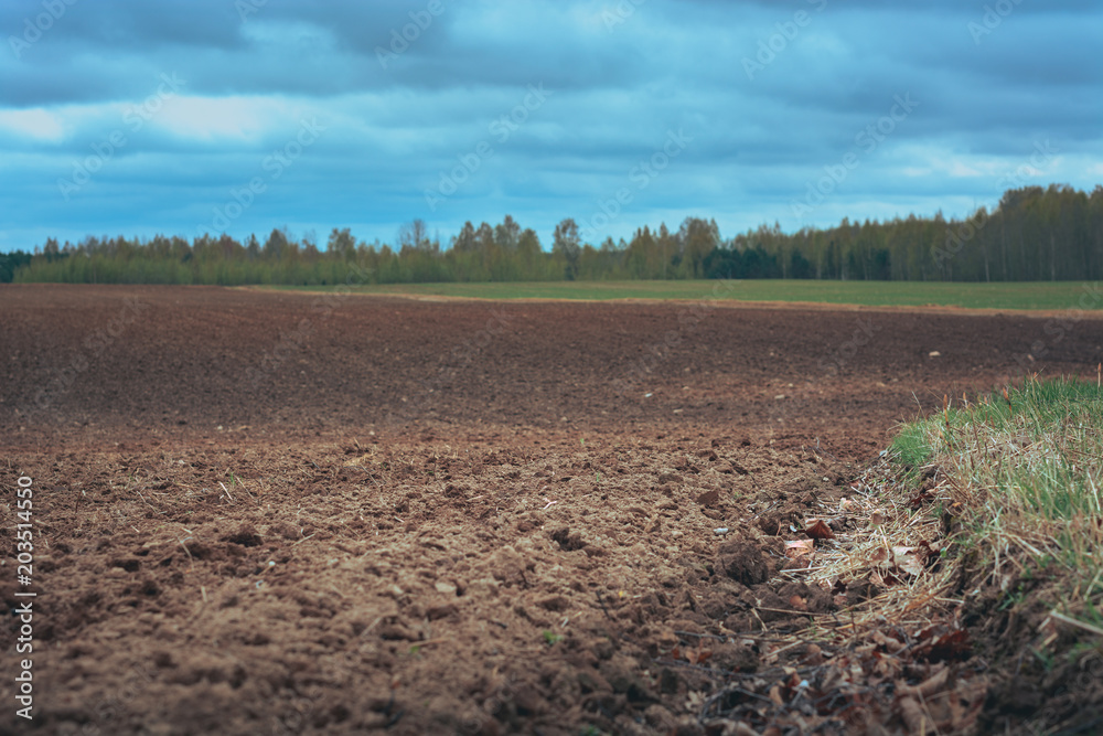 Tilled crop fields in a cloudy spring day. Texture in a freshly tilled soil surrounded by nature in bloom. Cultivated farm land in a vast territory. Stormy weather in country side. Tilled crop fields in a cloudy spring day. Texture in a freshly tilled soil surrounded by nature in bloom. Cultivated farm land in a vast territory. Stormy weather in country side.