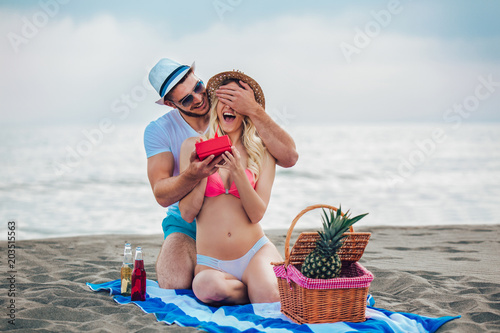 Young man suprising his girlfriend with gift on the beach photo