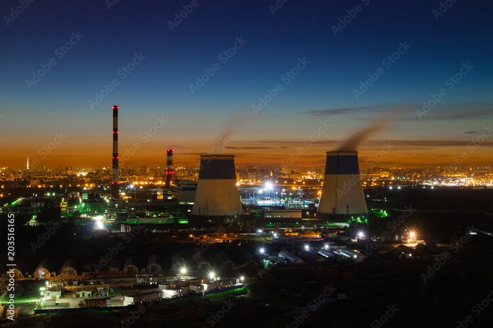 Industrial zone of the city in the evening. Boiler tube, sunset, night lights.