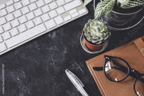 Flat lay. Office dark table with computer notepad, mouse, pen, paper clips, glasses, and smartphone. Top view angle with copy space.