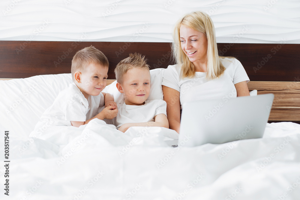 Young woman with her two kids using digital tablet in bed at home.