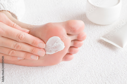 Groomed woman's hands applying feet moisturizing cream. Barefoot on the white towel. Cares about clean and soft legs skin. Healthcare concept.