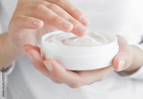 Beautiful groomed woman using moisturizing cream for clean and soft skin. Cream jar in hands. Healthcare concept. photo