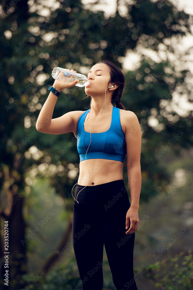 Woman with earphones drinking water after exercise Woman with earphones drinking water after exercise