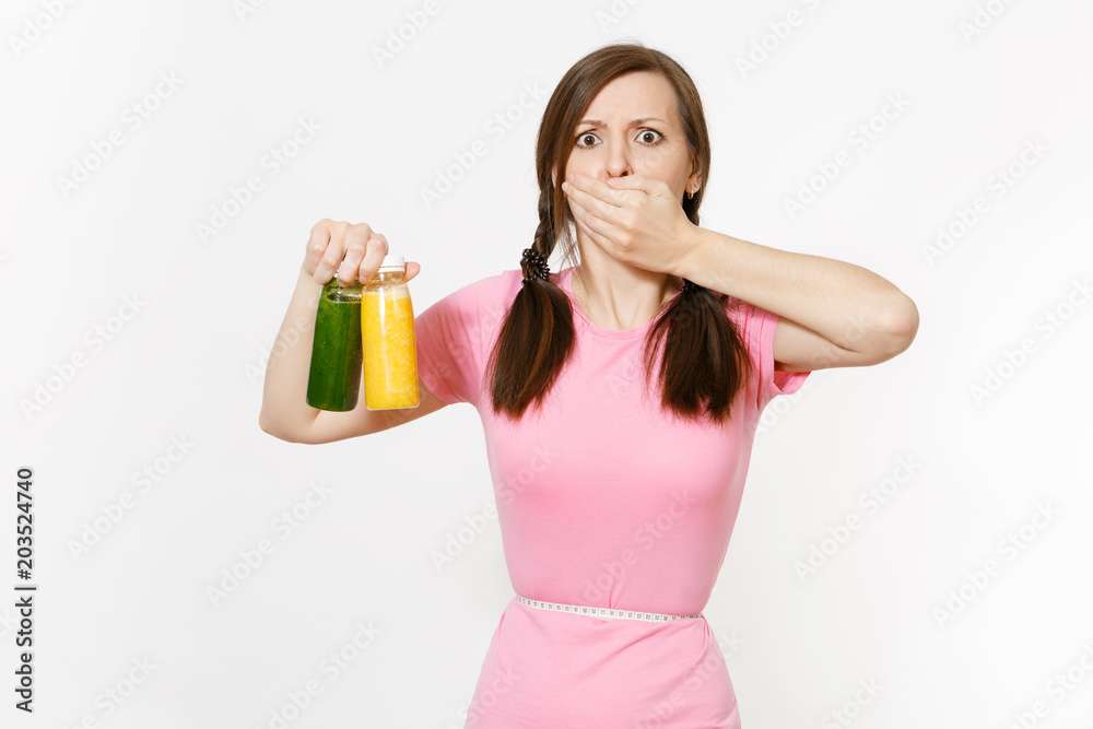 Sad woman holds green, yellow detox smoothies in bottles, measure tape on waist isolated on white background. Proper nutrition, vegetarian drink, healthy lifestyle, dieting concept. Copy space, flack. Sad woman holds green, yellow detox smoothies in bottles, measure tape on waist isolated on white background. Proper nutrition, vegetarian drink, healthy lifestyle, dieting concept. Copy space, flack.
