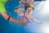 Mom teaches little girl with an open mouth swimming underwater in the pool