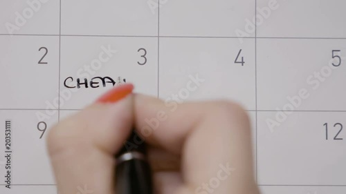Female hands planning diet and writing cheat day with capital letters and a smiley face on calendar with a black pen