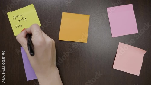 Top view of woman hands writing on colored sticky post it notes motivational quotes using black pen