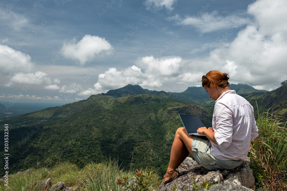 Caucasian girl working on her computer on the top of the mountain. Concept or remote work in internet for frilancer