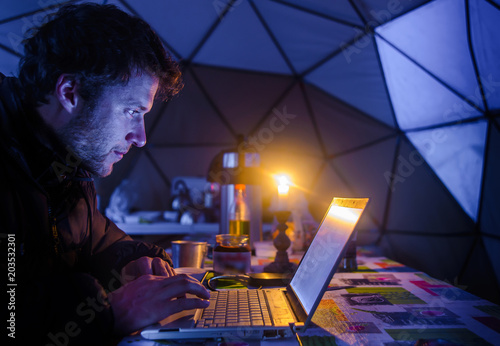 Man on expedition, using laptop in camp, Fletanes camp, Narsaq, Kitaa, Greenland photo