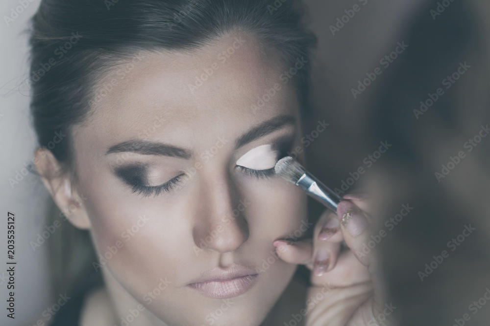 Obraz premium Young beautiful woman applying make-up by make-up artist. Process of making makeup.