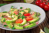 Vegetable salad with avocado, arugula, radish, lime and olive oil. Dietary healthy food. Wooden rustic background. Top view