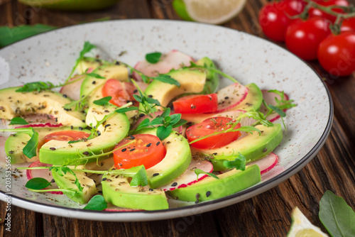 Vegetable salad with avocado, arugula, radish, lime and olive oil. Dietary healthy food. Wooden rustic background. Top view