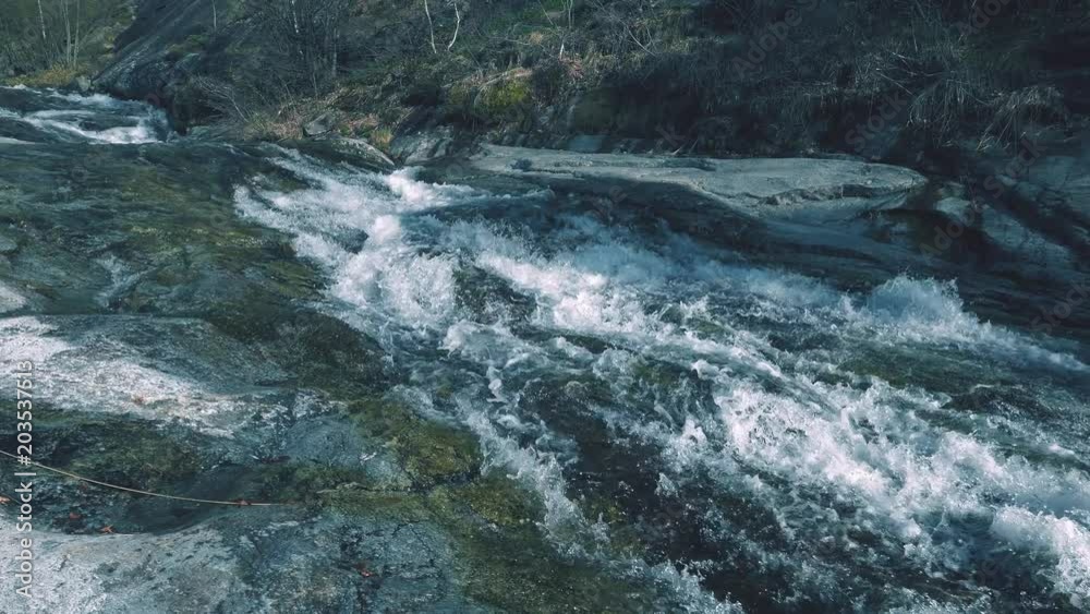 Alpine stream flowing on rock creating rapid and waterfall, clean fresh water in valley woodland, teal grading