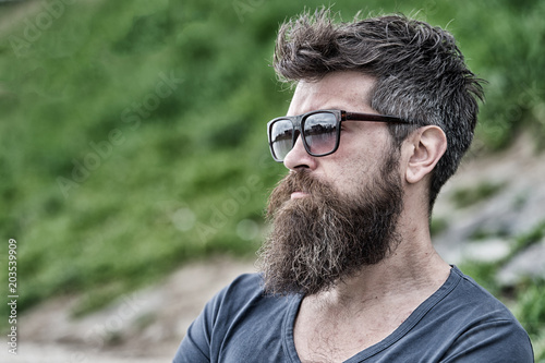 Man with beard and mustache on strict face, nature background, defocused. Bearded man wears modern sunglasses. Hipster with beard looks confident while standing outdoors. Barbershop and style concept. © be free