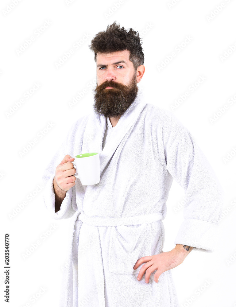 Man with beard and disheveled hair stands in bathrobe, holds mug with