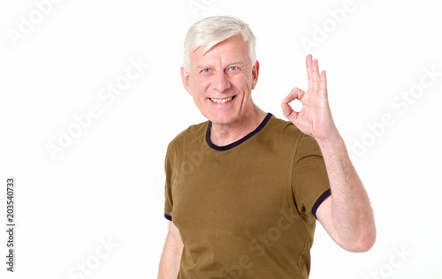 Portrait of a cheerful senior man showing okay gesture isolated on the white background. Adult man with gray hair shows his hand a character ok. © A Stock Studio