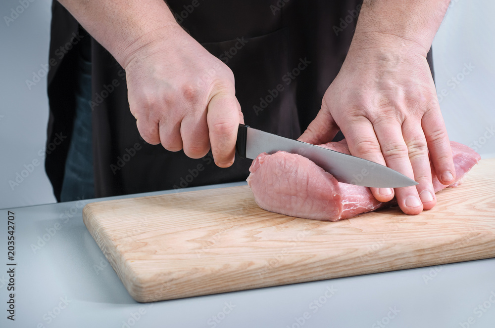 Butcher cutting fresh raw meat on a wooden cutting board